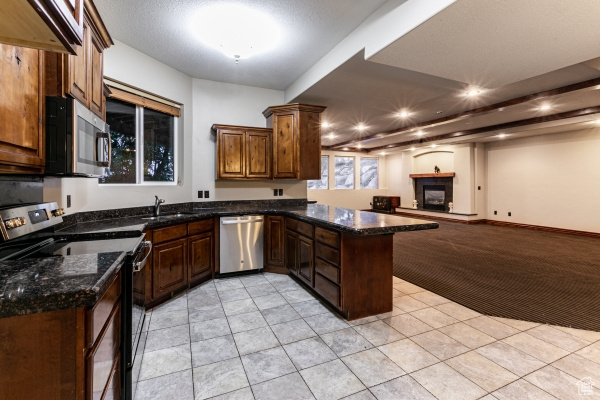 Kitchen with dark stone counters, light carpet, sink, appliances with stainless steel finishes, and kitchen peninsula