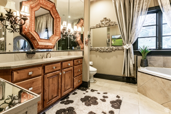 Bathroom featuring vanity, tile patterned flooring, toilet, and a relaxing tiled tub