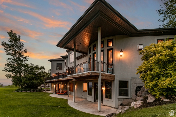 Back house at dusk with a balcony, a yard, and a patio area