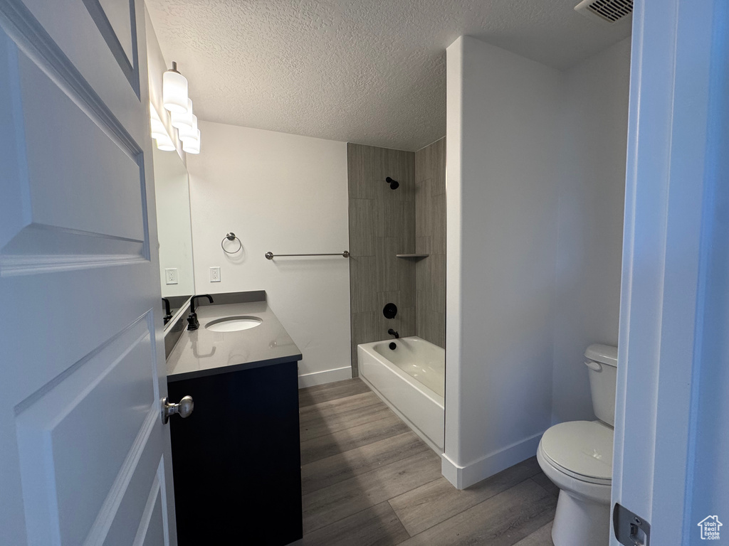 Full bathroom featuring toilet, hardwood / wood-style flooring, a textured ceiling, tiled shower / bath combo, and vanity