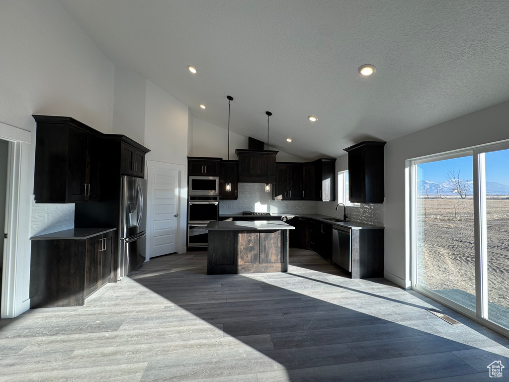 Kitchen with hardwood / wood-style flooring, hanging light fixtures, a kitchen island, backsplash, and appliances with stainless steel finishes