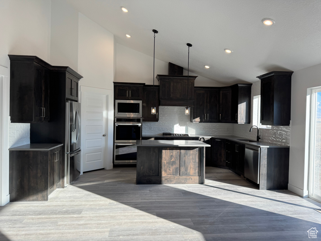 Kitchen featuring stainless steel appliances, pendant lighting, a kitchen island, sink, and tasteful backsplash