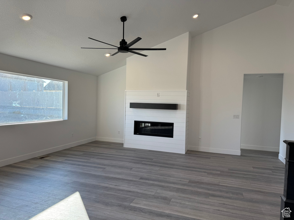 Unfurnished living room featuring ceiling fan, dark hardwood / wood-style flooring, lofted ceiling, and a fireplace