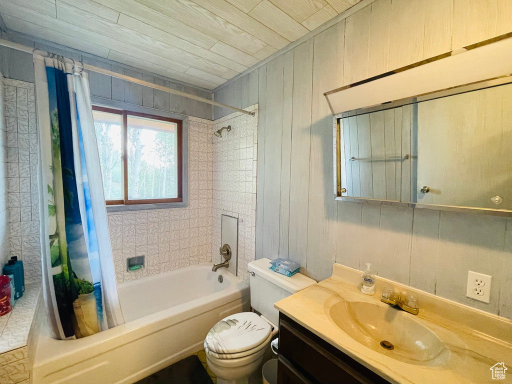 Full bathroom with shower / bath combo with shower curtain, wood walls, toilet, and vanity