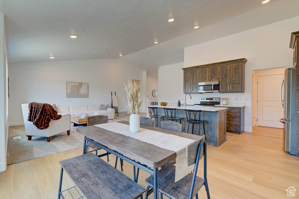 Dining space with light hardwood / wood-style flooring and high vaulted ceiling