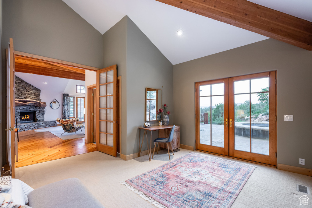 Doorway to outside with beam ceiling, french doors, light wood-type flooring, a stone fireplace, and high vaulted ceiling