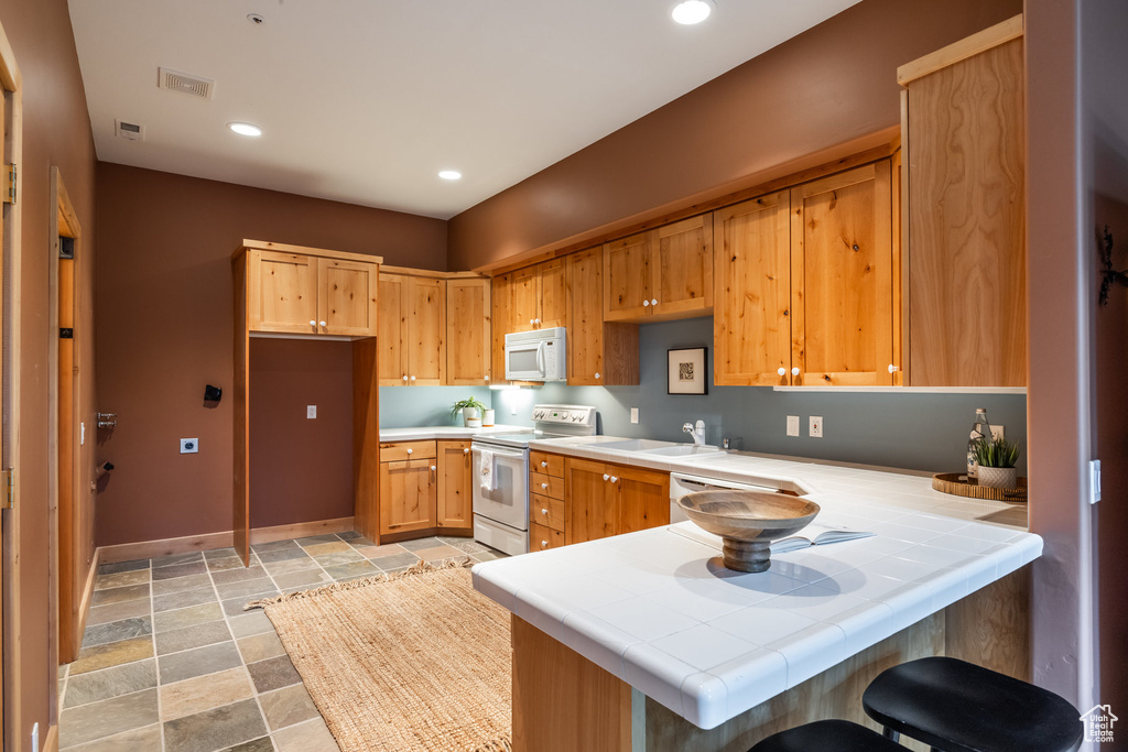 Kitchen featuring kitchen peninsula, white appliances, light tile patterned floors, and tile countertops