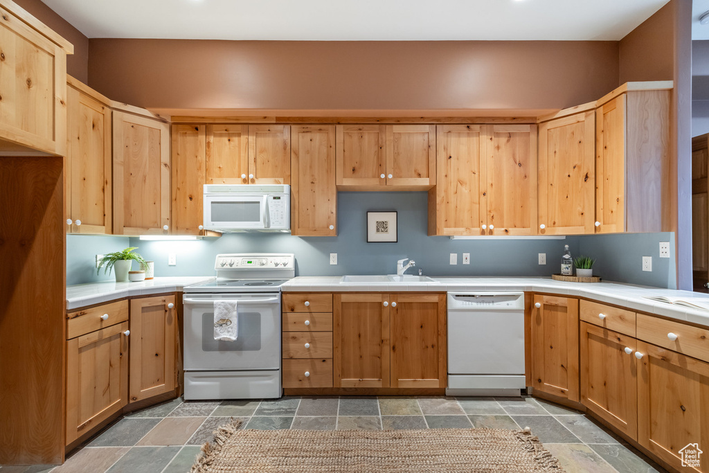 Kitchen featuring tile patterned flooring, light brown cabinetry, white appliances, and sink