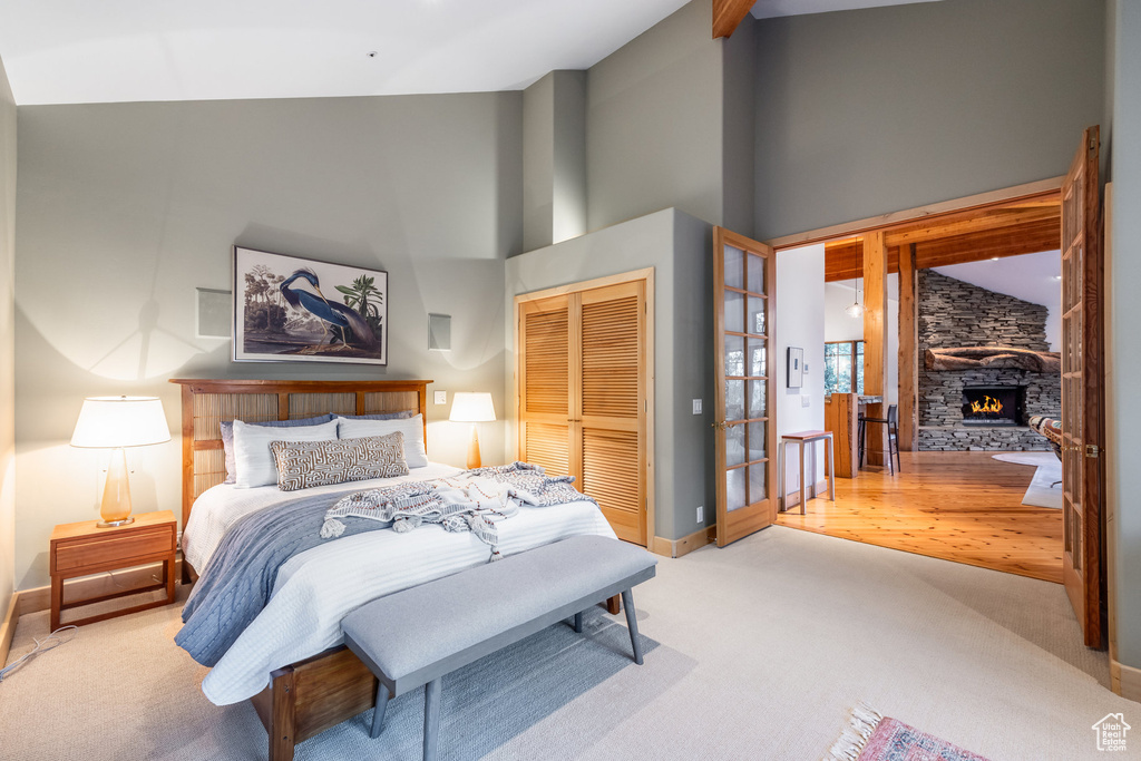 Bedroom with a stone fireplace, light carpet, a closet, and high vaulted ceiling