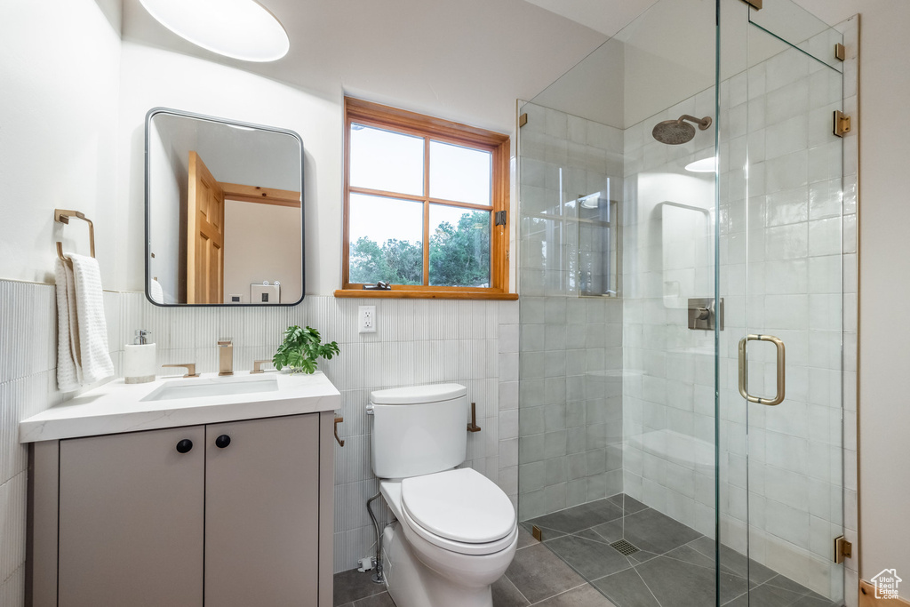 Bathroom with tile patterned flooring, a shower with door, toilet, vanity, and tile walls