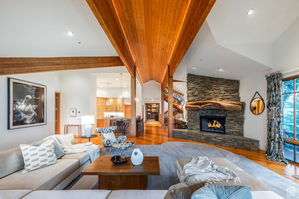 Living room featuring a stone fireplace, vaulted ceiling with beams, and light wood-type flooring