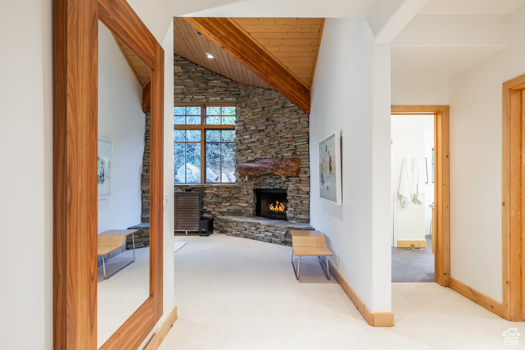 Living room with lofted ceiling with beams, carpet flooring, a stone fireplace, and wood ceiling