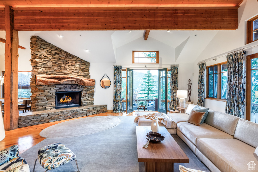 Living room featuring beamed ceiling, wood-type flooring, a stone fireplace, and high vaulted ceiling