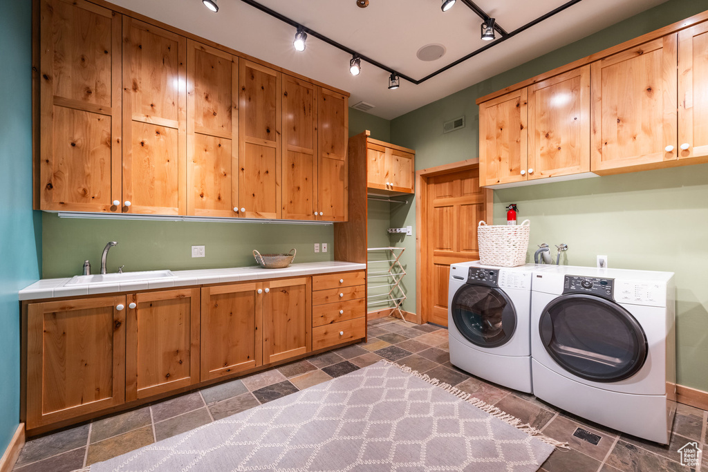 Clothes washing area featuring washer and dryer, track lighting, cabinets, dark tile patterned flooring, and sink