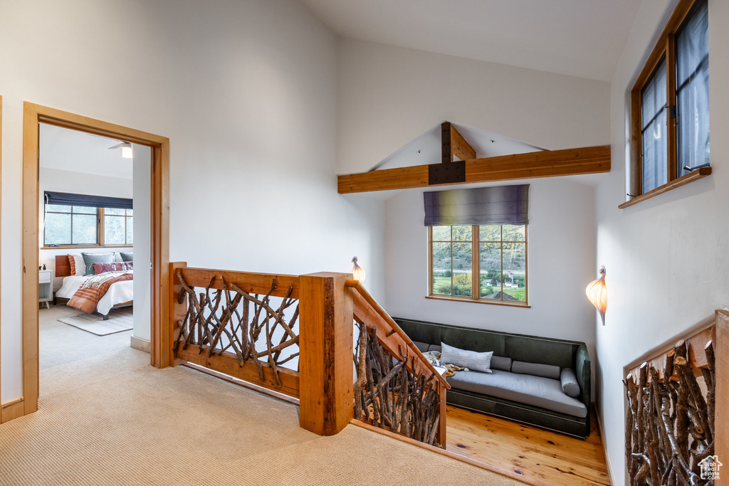 Hall with beamed ceiling, light carpet, a wealth of natural light, and high vaulted ceiling