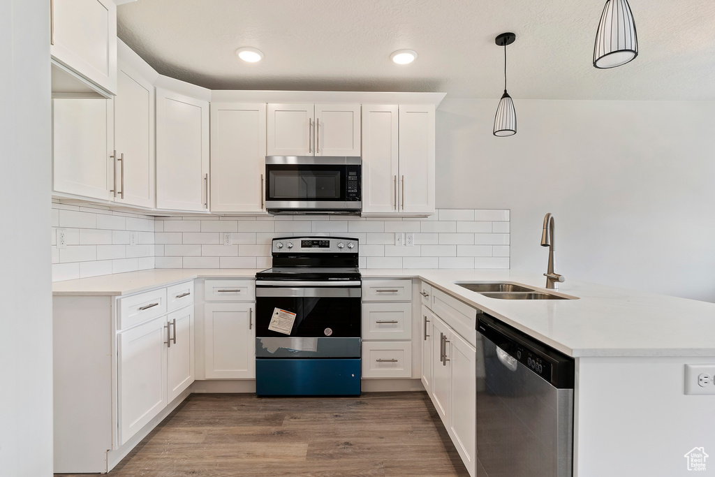 Kitchen with sink, appliances with stainless steel finishes, wood-type flooring, and white cabinetry