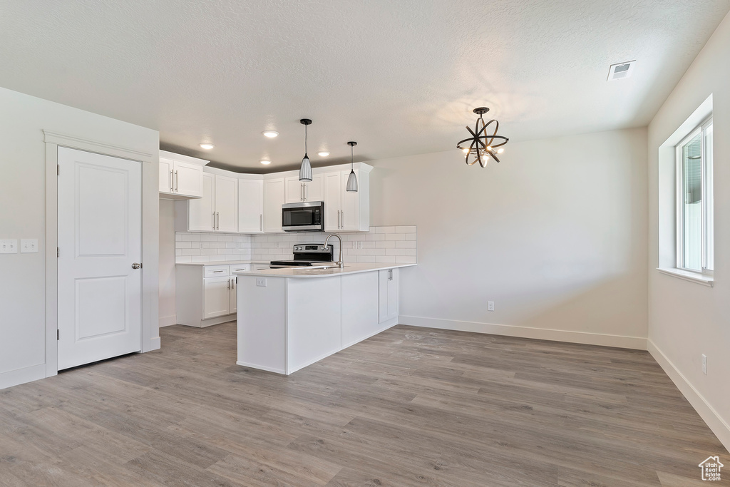 Kitchen with stainless steel appliances, white cabinets, kitchen peninsula, hanging light fixtures, and light wood-type flooring