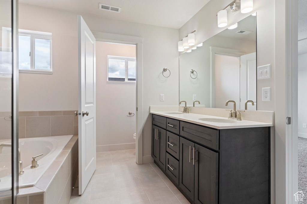 Bathroom with dual vanity, tile patterned floors, and a relaxing tiled tub