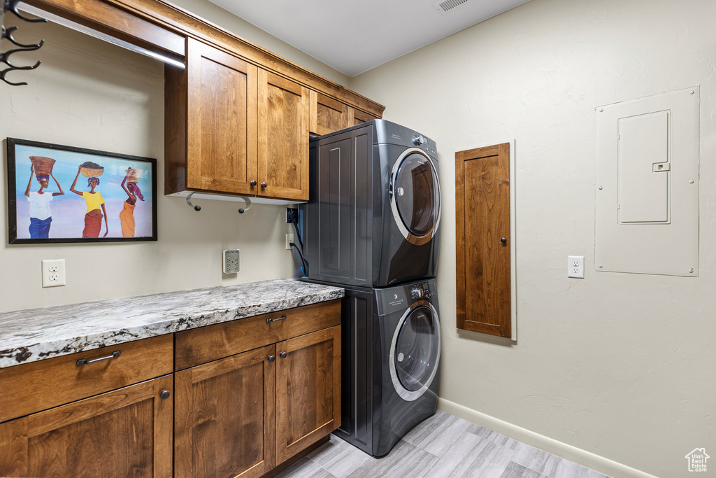 Laundry area featuring electric panel, light hardwood / wood-style flooring, stacked washer and clothes dryer, and cabinets