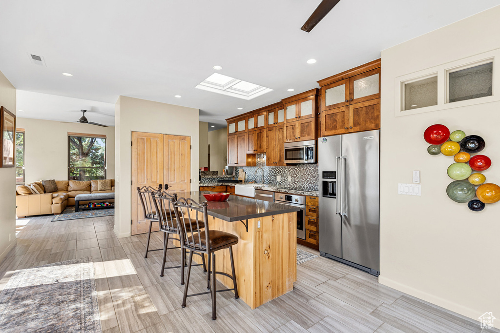 Kitchen featuring appliances with stainless steel finishes, a skylight, ceiling fan, decorative backsplash, and a breakfast bar area