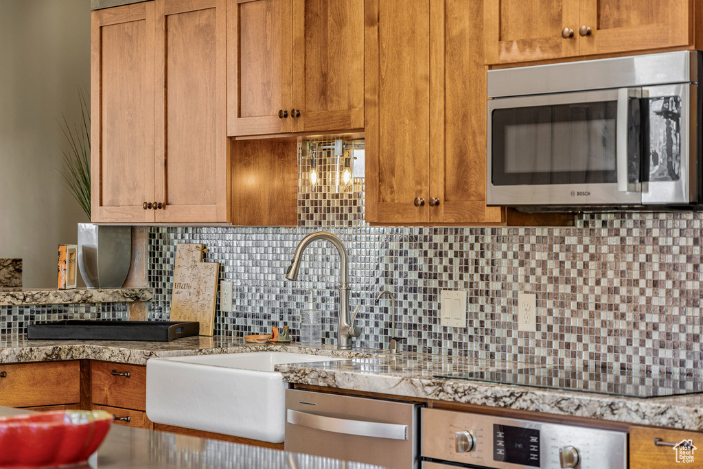 Kitchen featuring appliances with stainless steel finishes, tasteful backsplash, sink, and light stone counters