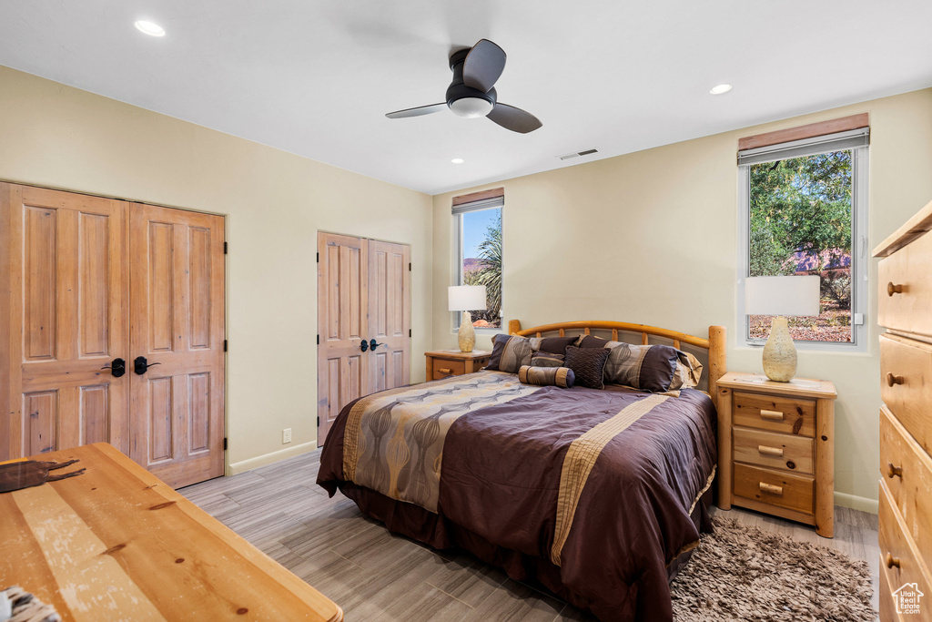 Bedroom with ceiling fan, light hardwood / wood-style flooring, and two closets