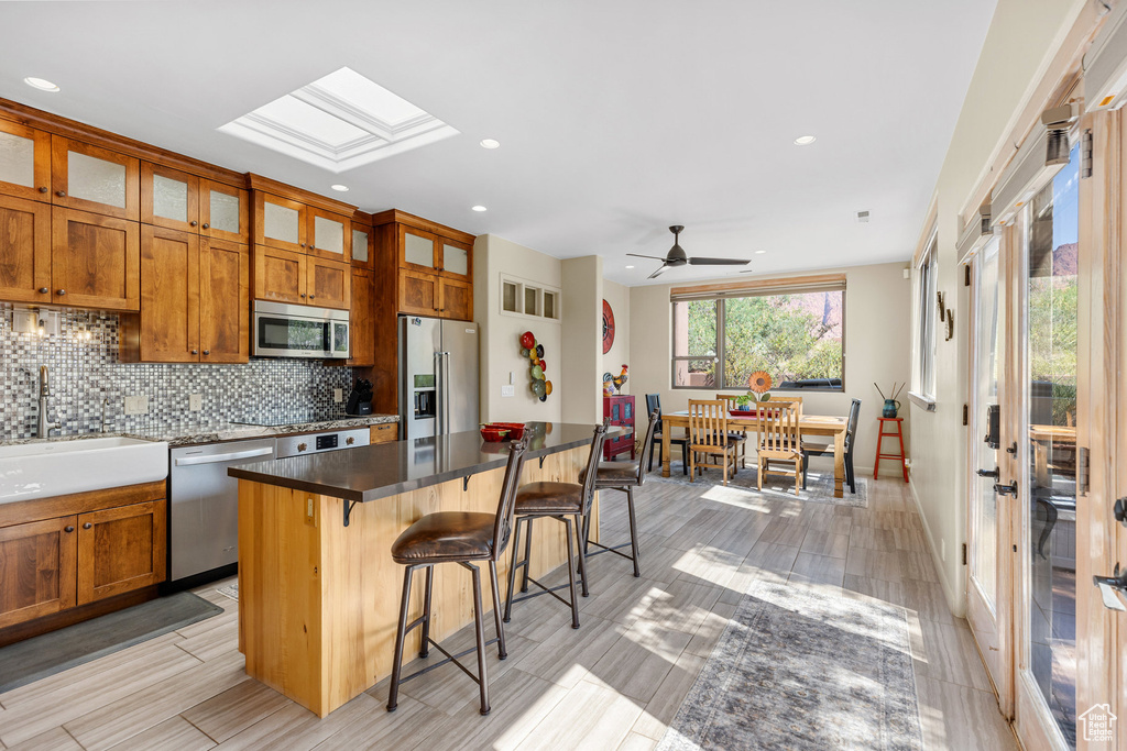 Kitchen with appliances with stainless steel finishes, a skylight, light wood-type flooring, a kitchen bar, and a center island