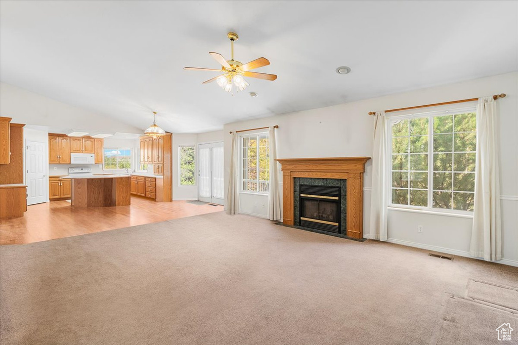 Unfurnished living room featuring ceiling fan, light colored carpet, vaulted ceiling, and a high end fireplace