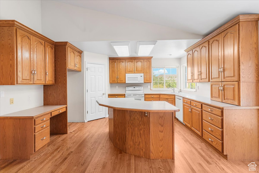 Kitchen with vaulted ceiling, a center island, light wood-type flooring, and white appliances