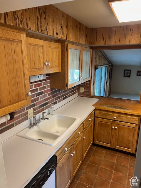 Kitchen with dark tile patterned floors, backsplash, dishwasher, and sink