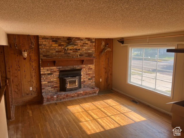 Unfurnished living room with wood walls, a textured ceiling, a fireplace, and light wood-type flooring