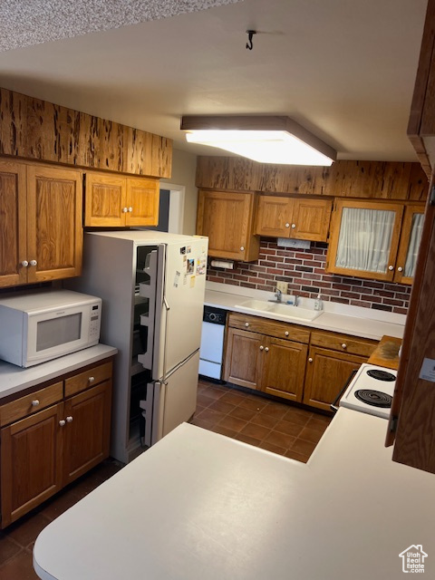 Kitchen with tasteful backsplash, white appliances, dark tile patterned flooring, vaulted ceiling, and sink