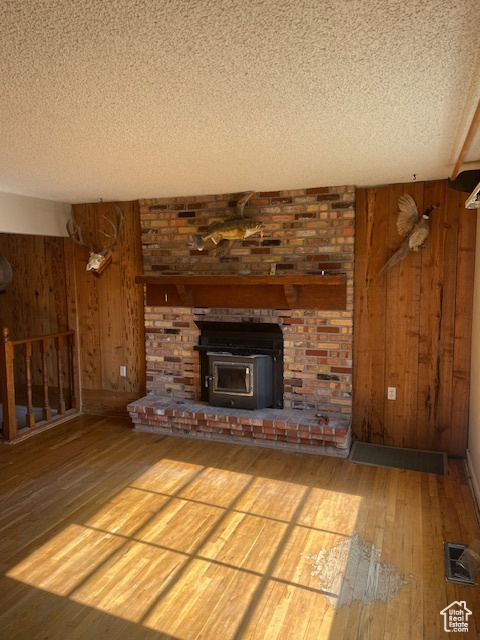 Unfurnished living room with a brick fireplace, a textured ceiling, wooden walls, and light hardwood / wood-style floors