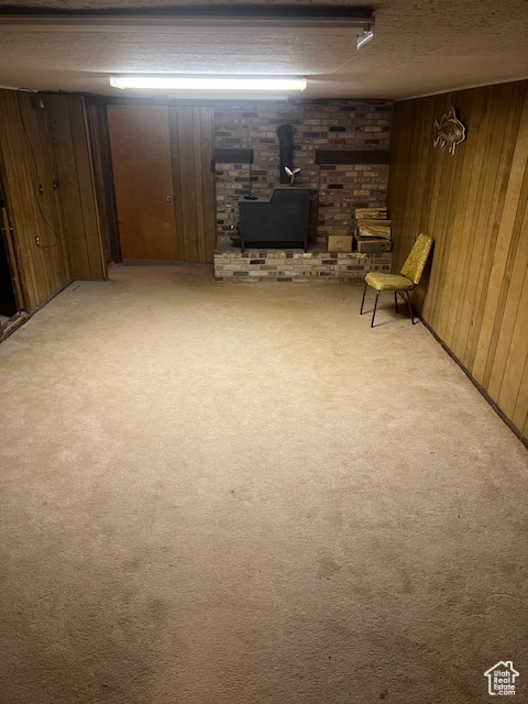 Basement featuring brick wall, a wood stove, light carpet, and wooden walls