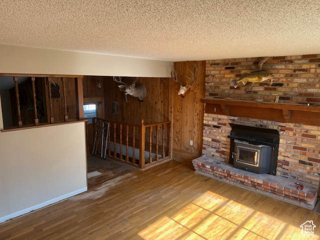 Unfurnished living room with a wood stove, wooden walls, a textured ceiling, hardwood / wood-style floors, and a fireplace