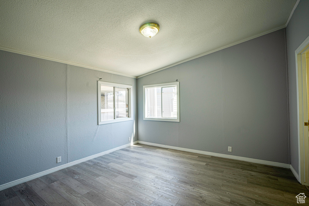 Unfurnished room with lofted ceiling, wood-type flooring, ornamental molding, and a textured ceiling