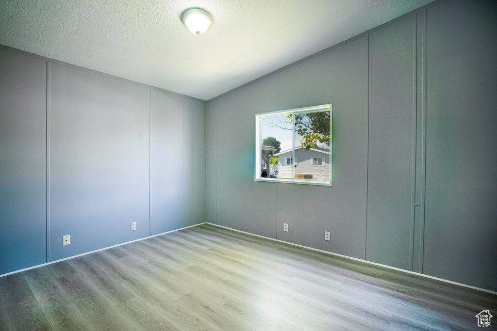 Unfurnished room with wood-type flooring, vaulted ceiling, and a textured ceiling