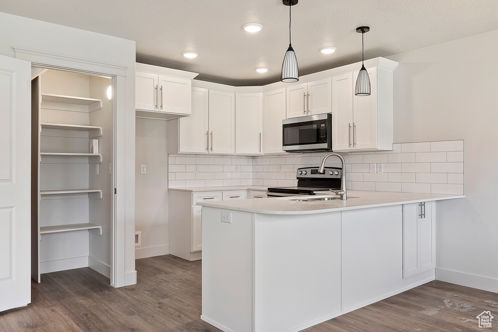 Kitchen with hardwood / wood-style flooring, tasteful backsplash, appliances with stainless steel finishes, and kitchen peninsula