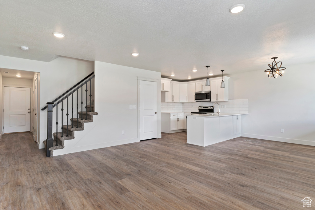 Kitchen featuring stainless steel appliances, white cabinets, kitchen peninsula, decorative light fixtures, and wood-type flooring