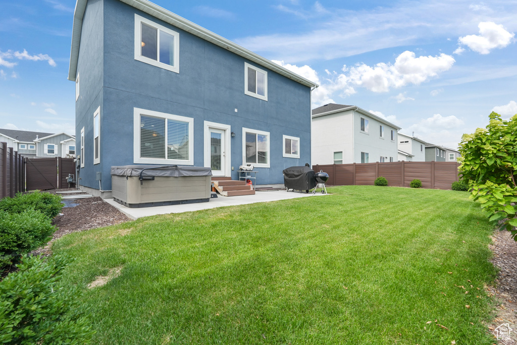 Rear view of property featuring a patio, a hot tub, and a yard