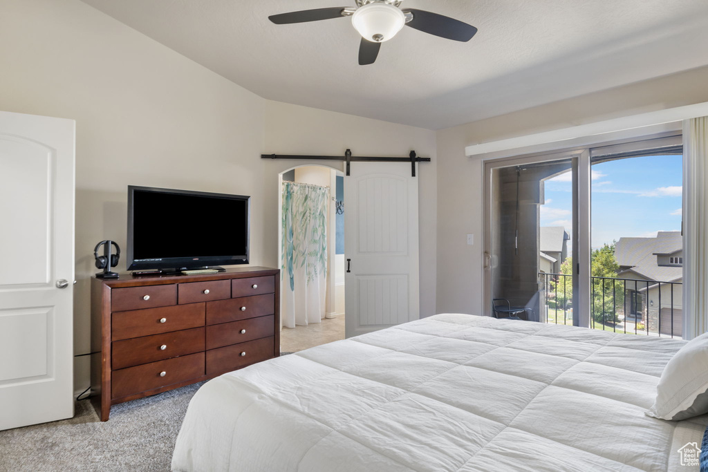 Carpeted bedroom featuring a barn door, access to outside, ceiling fan, and vaulted ceiling