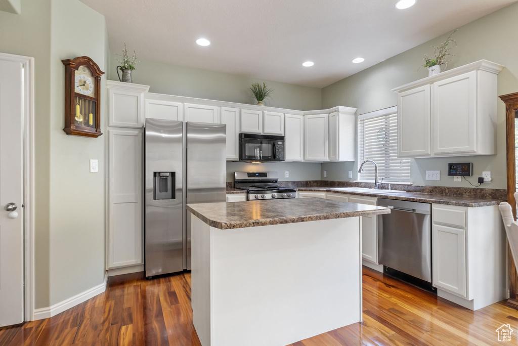 Kitchen with appliances with stainless steel finishes, a center island, wood-type flooring, and sink