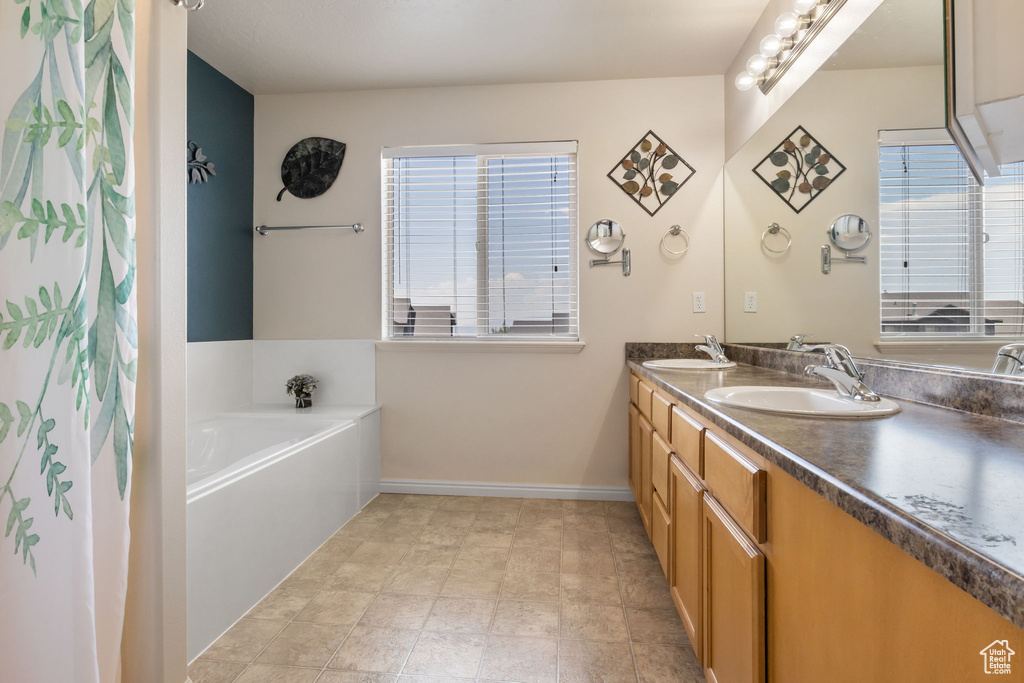 Bathroom featuring a washtub, dual vanity, tile patterned floors, and plenty of natural light