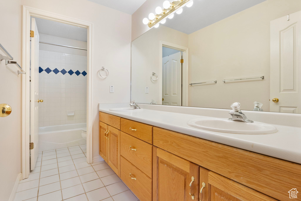 Full bathroom with tiled shower / bath combo, toilet, tile patterned flooring, and double sink vanity