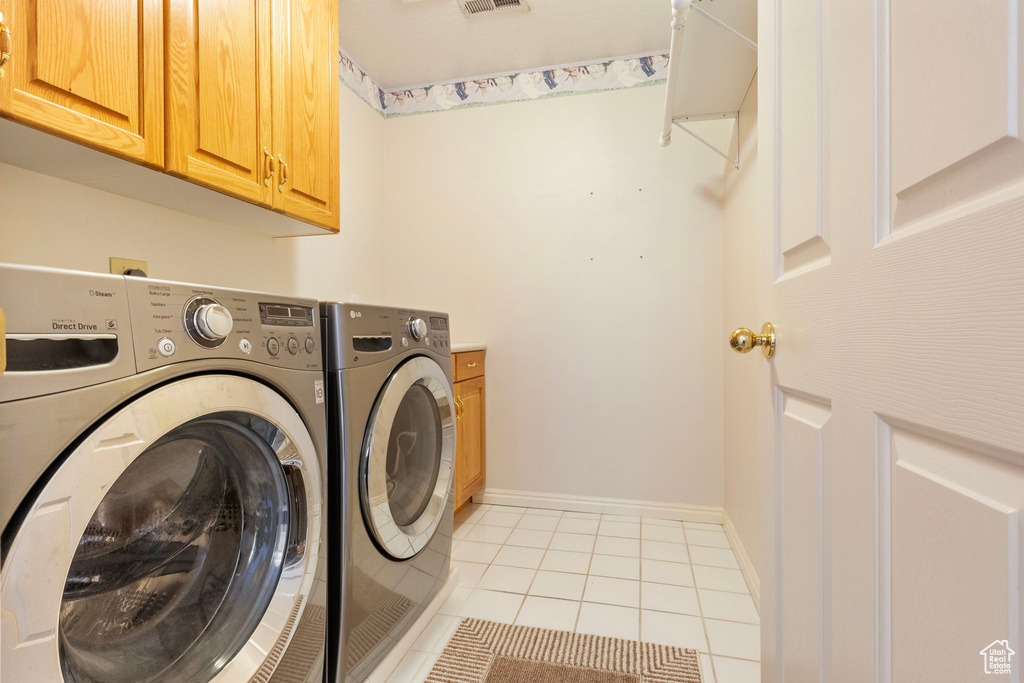 Clothes washing area featuring light tile patterned flooring, washer and dryer, and cabinets