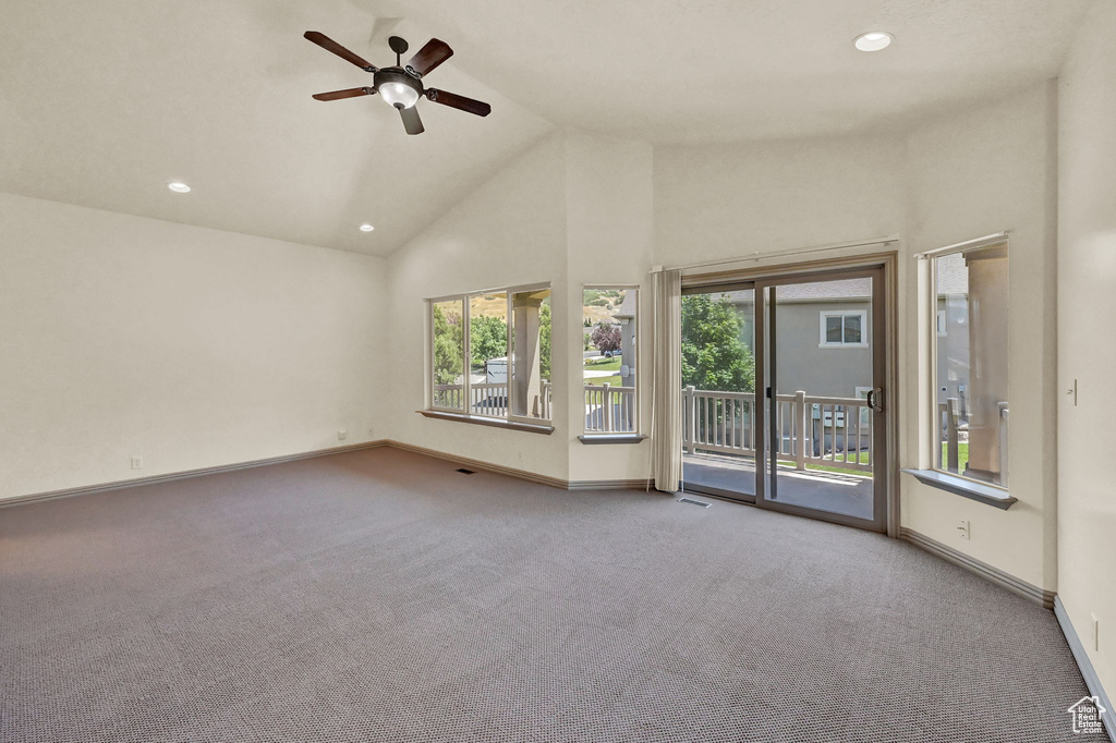 Carpeted empty room featuring ceiling fan, high vaulted ceiling, and plenty of natural light