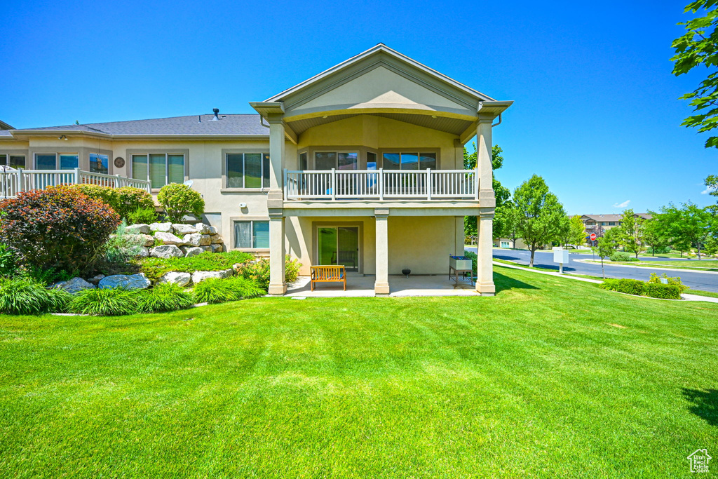 Back of property featuring a balcony, a patio area, and a lawn