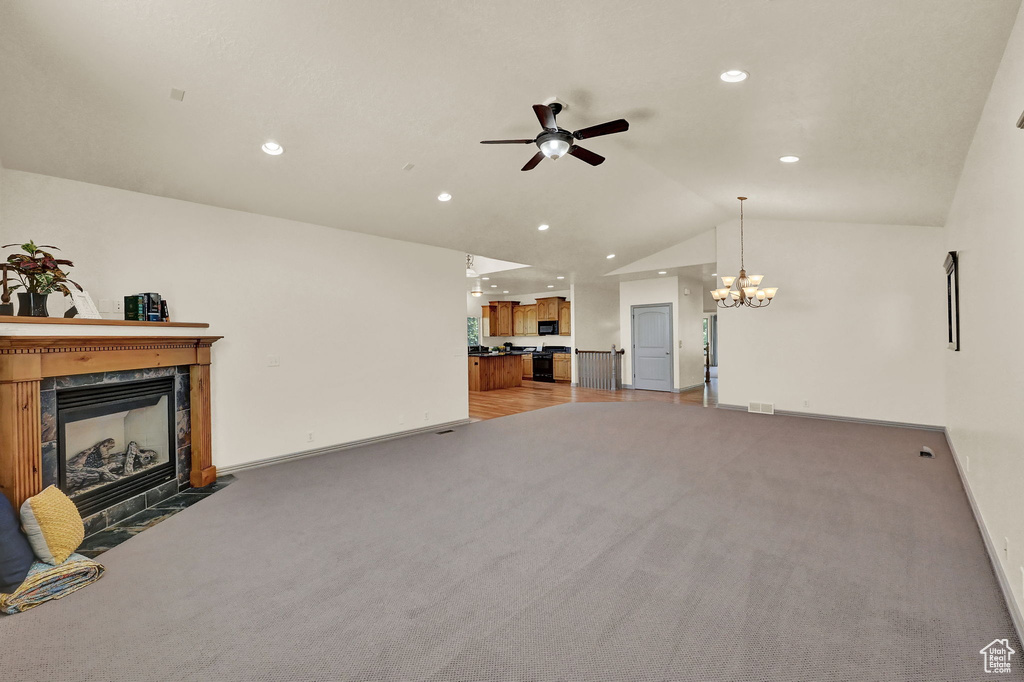 Unfurnished living room with lofted ceiling, ceiling fan with notable chandelier, carpet, and a fireplace