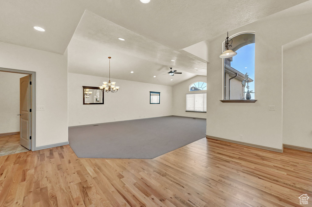 Unfurnished living room with light hardwood / wood-style flooring, ceiling fan with notable chandelier, and lofted ceiling