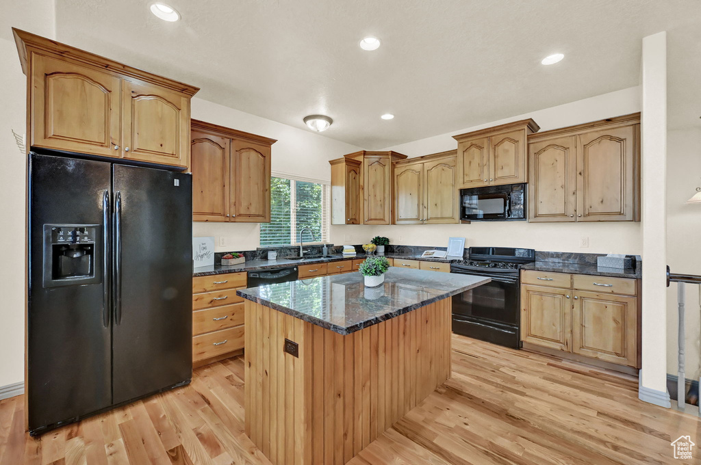 Kitchen with dark stone counters, black appliances, sink, light wood-type flooring, and a center island